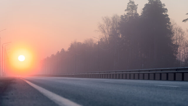 Sunrise, in the foreground, the road passing through the forest is covered with a thin layer of fog