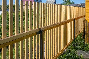 Close-up of a new wooden picket fence in the backyard of a country house, a sunny summer day