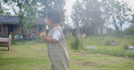 A young child is holding a yellow flower in a field. The scene is peaceful and serene, with the child standing in the grass and the flower in their hand