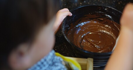A child is making a homemade dessert chocolate cake with a parent. The child is holding a spoon...