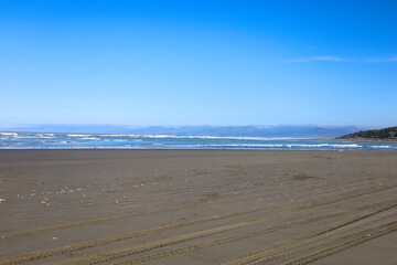 Sehr breiter Sandstrand in Neuseeland auf der Südinsel mit blick aufs Wasser und Spuren von Autos im Sand
