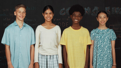 Group of smart multicultural teenager looking at camera at blackboard. Happy diverse children...
