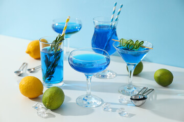 Blue drink in cocktail glasses, lemons, limes and ice cubes on blue background