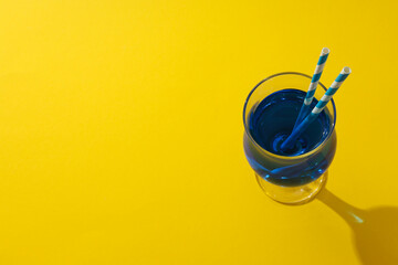 Blue cocktail with straws in glass on yellow background, space for text