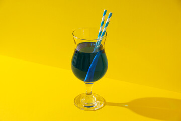 Blue cocktail with straws in glass on yellow background