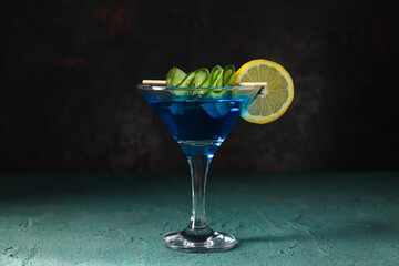 Blue cocktail with lemon and cucumber slices in glass on dark gray background, close up