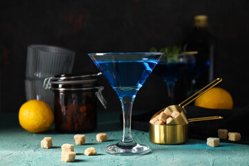Blue cocktail in glass, lemon, sugar cubes and tools on dark background