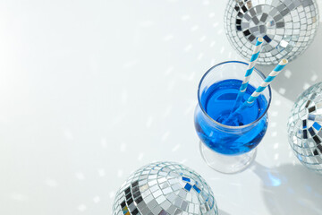 Blue cocktail with straws in glass and disco balls on white background, space for text