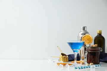 Blue cocktail in glass, oranges slices, bottles and ice cubes on white background, space for text