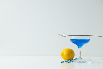Blue cocktail in glass, whole lemon, spoon, straws and ice cubes on white background, space for text