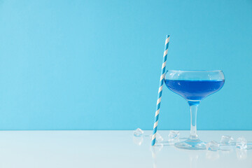 Blue cocktail in glass, straw and ice cubes on blue background, space for text