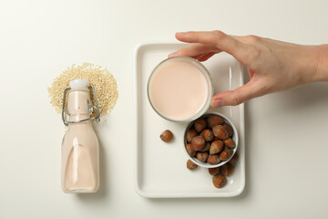 Bottle and glass with milk, hand, sesame seeds and nuts in bowl on white background, top view