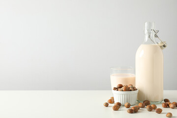 Bottle and glass with milk, bowl with nuts on white background, space for text