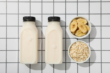 Bottles with milk and bowls with oatmeal and sliced bananas on light background, top view
