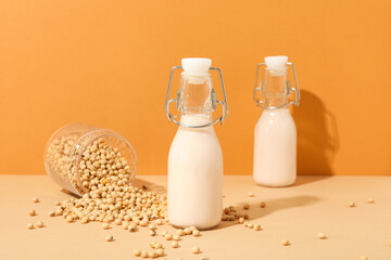 Bottles of alternative milk and soybeans on orange background