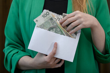 Elegancka kobieta trzyma w dłoni kopertę z polskimi pieniędzmi 