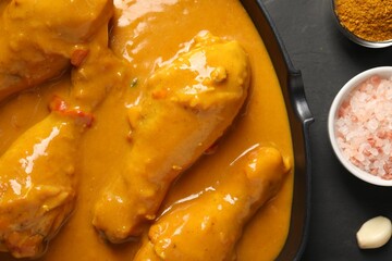 Tasty chicken curry and ingredients on black textured table, flat lay
