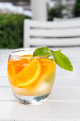 Citrus and mint leaves infused water, cocktail, lemonade in glass. Summer iced cold drink with orange, ice and mint on white wooden striped background, copy space, side view, hard shadows, vertical
