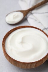 Delicious natural yogurt in bowl and spoon on light grey table, closeup