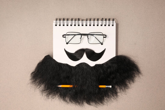 Flat lay composition with artificial moustache and glasses on light brown background