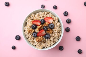 Tasty oatmeal with strawberries, blueberries and walnuts in bowl surrounded by fresh berries on pink background, flat lay