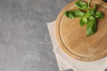 Wooden cutting board, fresh basil and napkin on grey table, top view. Space for text