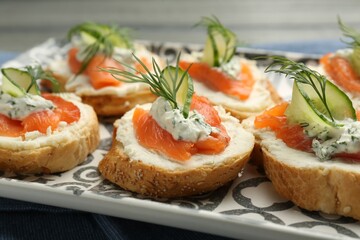 Tasty canapes with salmon, cucumber, cream cheese and dill on table, closeup