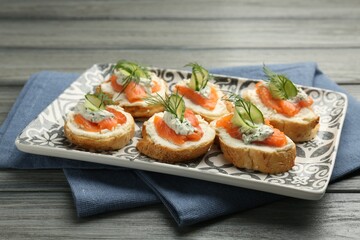 Tasty canapes with salmon, cucumber, cream cheese and dill on wooden table