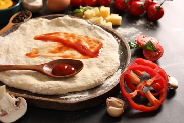 Pizza dough with tomato sauce and products on dark table, closeup