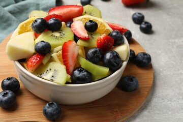 Tasty fruit salad in bowl and ingredients on gray table, closeup