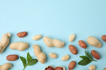 Fresh peanuts and leaves on light blue table, flat lay. Space for text