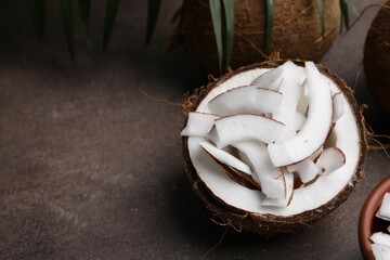Coconut pieces in nut shell on brown table, space for text