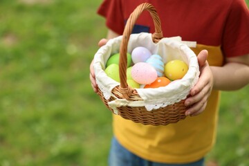 Easter celebration. Little boy holding basket with painted eggs outdoors, closeup. Space for text