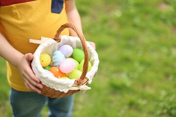 Easter celebration. Little boy holding basket with painted eggs outdoors, closeup. Space for text