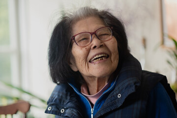 An elderly woman in her nineties laughs while turning to talk to someone standing next to her. She...