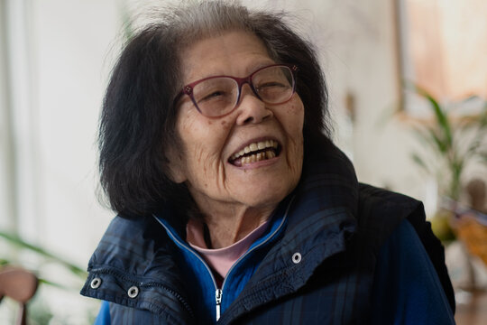 An elderly woman in her nineties laughs while turning to talk to someone standing next to her. She is Asian, of Okinawan (Ryukyuan) descent.