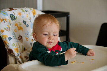 Naklejka premium Adorable little baby girl sitting in high chair and eating