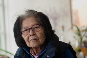 An elderly woman looks seriously at the camera. She is leaning to the side, with a warm vest on....