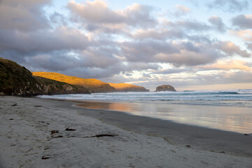 Wunderschöner Strand im Süden von Neuseeland im Sonnenuntergang mit Wellen und Wolken