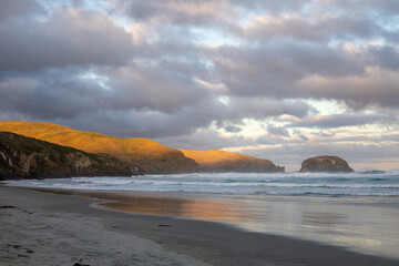 Wunderschöner Strand im Süden von Neuseeland im Sonnenuntergang mit Wellen und Wolken