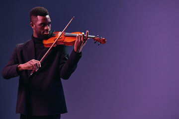 Elegant musician in black suit playing violin on purple background with copy space