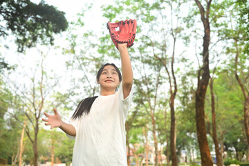 Happy smiling teenage Asian girl wearing leather glove playing baseball at public park