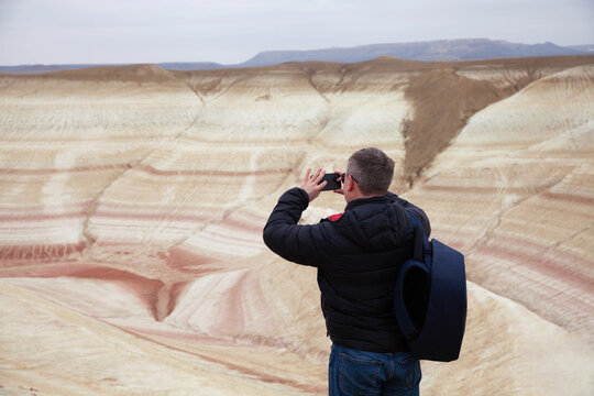 Man in a black jacket stands before Tiger-striped hills, observing the patterned landscape