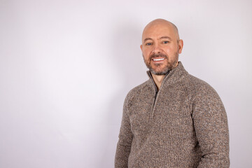 A middle aged bald shaven headed man with a beard smiling wearing a jumper on white background