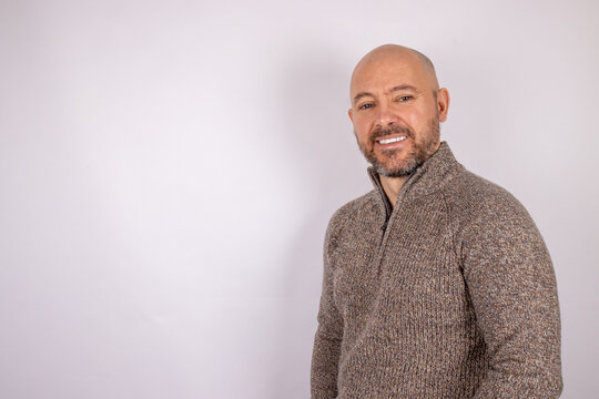 A middle aged bald shaven headed man with a beard smiling wearing a jumper on white background