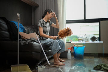 Young housewife sitting on sofa with cleaning tools feeling tired after doing housework