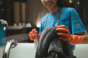 Woman in rubber gloves cleaning bathtub and faucet in a modern bathroom. Cleaning service concept