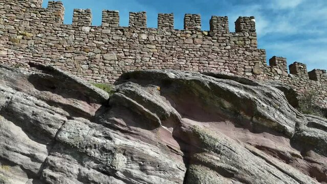 Aerial drone view of the walls and tower of a stoney castle in the top of a rocky hill in Guadalajara, Spain. Drone flying down, camera tilting up. 4K