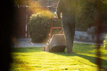 Garden worker with lawn mover. Garden works in spring. - obrazy, fototapety, plakaty