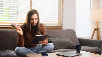 Young caucasian woman holding a credit card and purchasing online on digital tablet